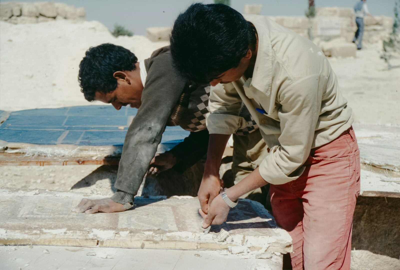 Two young men working on stone blocks outdoors.