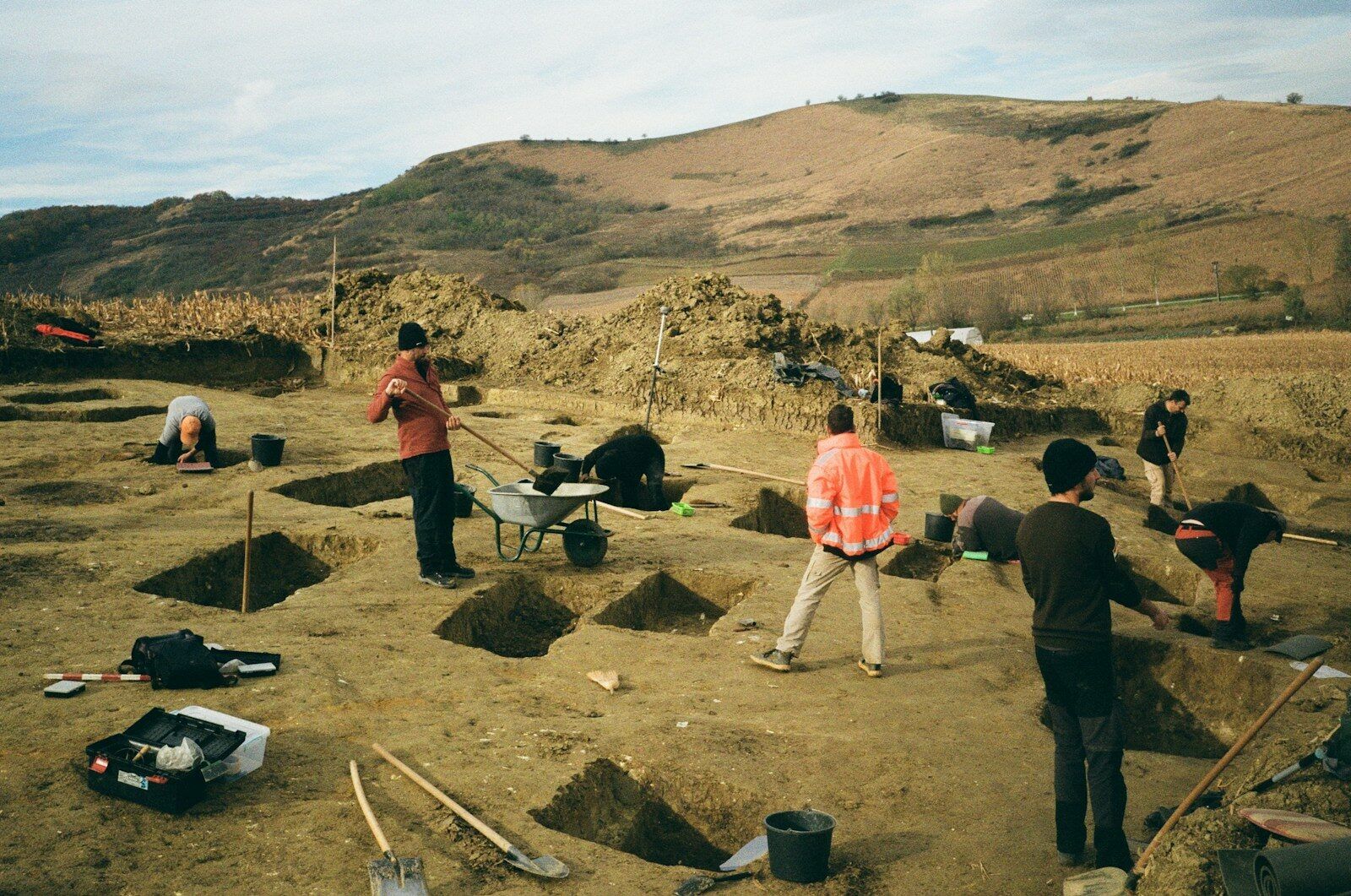 Archaeologists excavating a field with tools and trenches.